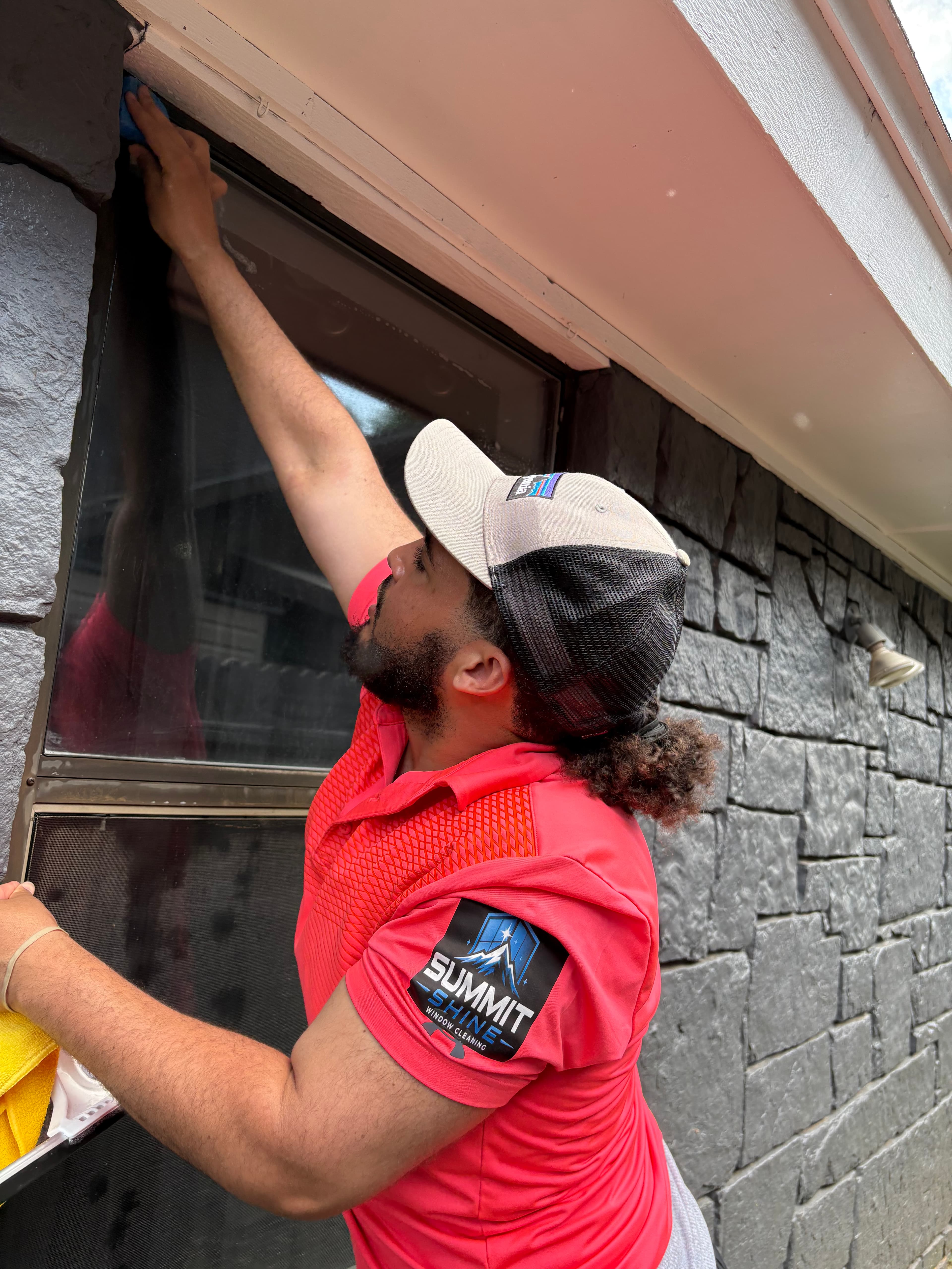 Professional cleaner in a pink shirt wipes the top corner of an exterior window frame.